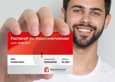 © Ei Electronics Mann, der die Zertifizierung in Scheckkartenform in die Kamera hält.