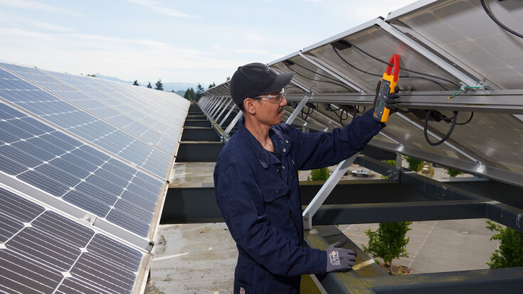 © Fluke Techniker, der die Messzange an eine Freiflächen-PV-Anlage hält.