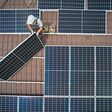 Men workers installing photovoltaic solar moduls on roof of house. Engineers in helmet building solar panel system outdoors. Concept of alternative and renewable energy. Aerial view.