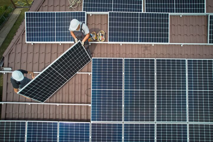 Men workers installing photovoltaic solar moduls on roof of house. Engineers in helmet building solar panel system outdoors. Concept of alternative and renewable energy. Aerial view.