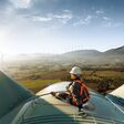 Happy engineer feel success after good work. He standing a top of windmill and looking beautiful sunset landscape