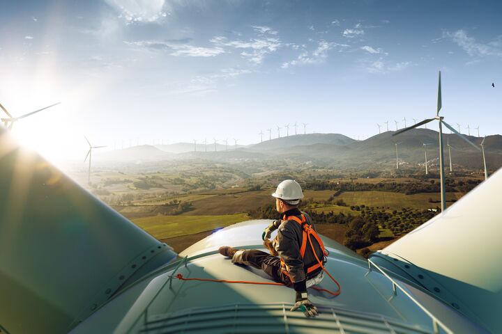 Happy engineer feel success after good work. He standing a top of windmill and looking beautiful sunset landscape