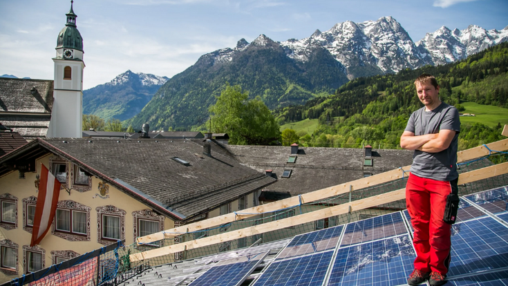 © ekt Klaus Hohenwarter Eine Dachfläche mit PV-Modulen in ländlicher Umgebung. Ein Mann steht auf dem Dach, im Hintergrund ist eine Kirche sichtbar.