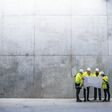 A group of engineers standing against concrete wall on construction site, holding blueprints. Copy space.