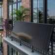 Balcony black satin solar panel on brick apartment with distant waterfront cranes, Tampa, Florida, USA