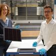 Projektleiterin Laura Stevens zeigt eines der III-V-Germanium-PV-Module mit einer Rekordeffizienz von 34,2 Prozent. Leonhard Böck ist Projektmitarbeiter und hat maßgeblich am – vor ihm liegenden – III-V-Silizium-PV-Modul mit 31,3 Prozent Effizienz mitgearbeitet.