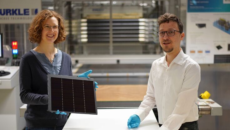 Projektleiterin Laura Stevens zeigt eines der III-V-Germanium-PV-Module mit einer Rekordeffizienz von 34,2 Prozent. Leonhard Böck ist Projektmitarbeiter und hat maßgeblich am – vor ihm liegenden – III-V-Silizium-PV-Modul mit 31,3 Prozent Effizienz mitgearbeitet.