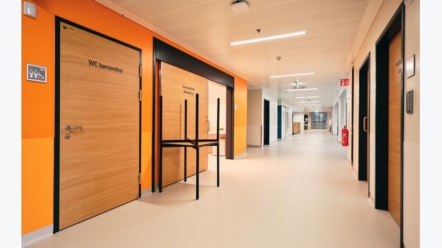 In den Fluren unterstützt die Kombination aus warmen Wandfarben und hellen Deckenleuchten die Patient*innen bei ihrer Genesung